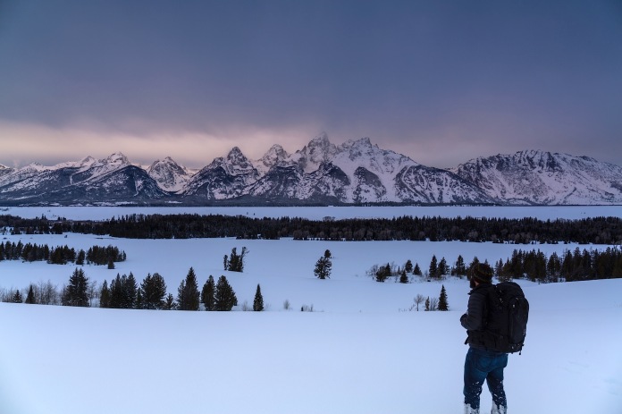 Lone male hiker looking out in the snow toward the tetons